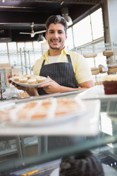 Trabajador sonriente mostrando plato de magdalenas —  Fotos de Stock