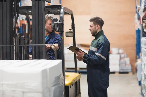 Warehouse worker talking with forklift driver — Stock Photo, Image