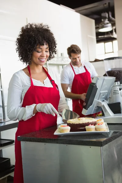 Serveerster snijden taart met ober achter haar — Stockfoto