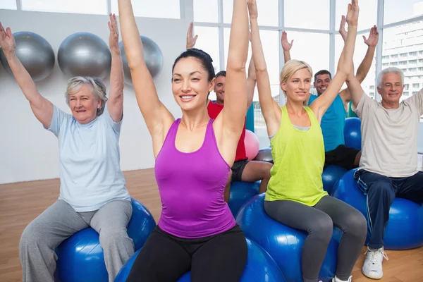 Menschen sitzen mit erhobenen Händen auf Gymnastikbällen — Stockfoto