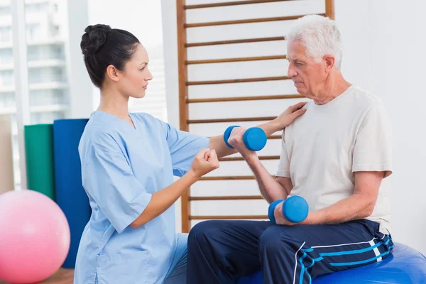 Trainer assisting man in lifting dumbbells — Stock Photo, Image
