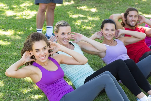 Fitness groep doen sit ups in park met coach — Stockfoto