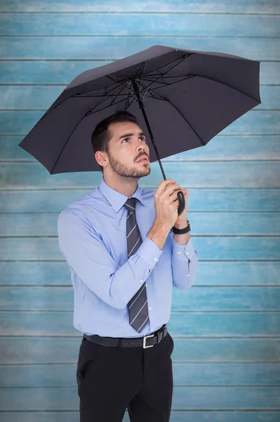 Anxious businessman sheltering with umbrella — Stock Photo, Image