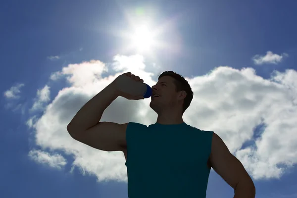 Человек пьет воду против голубого неба — стоковое фото