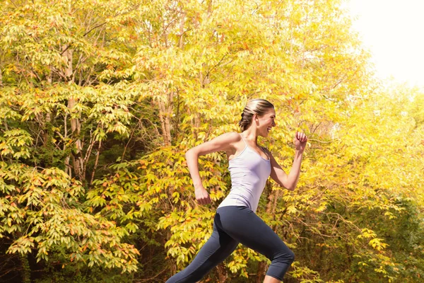 In forma bionda jogging contro foresta autunnale — Foto Stock