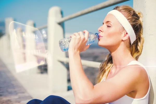 Fit blonde sitting on pier drinking water — Stock Photo, Image