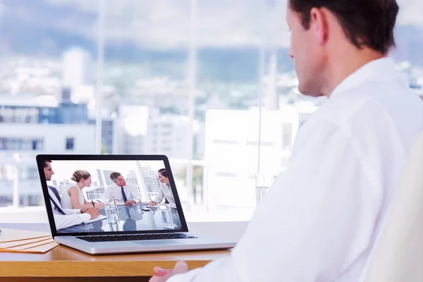 Empresário olhando para um laptop contra reunião — Fotografia de Stock