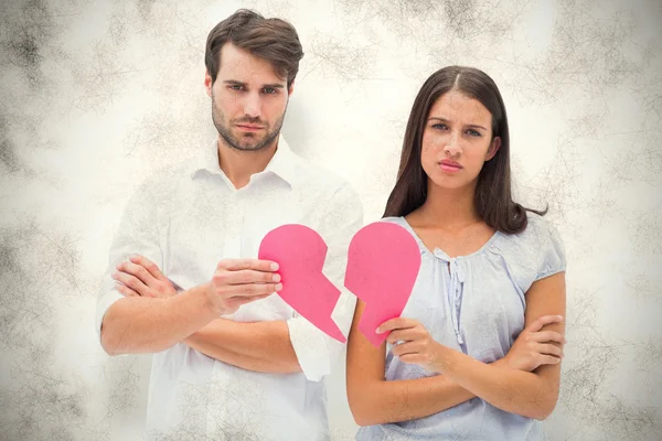 Composite image of upset couple holding two halves of broken hea — Stock Photo, Image