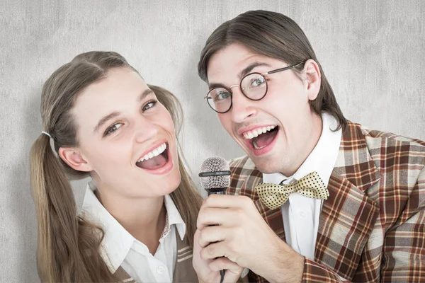 Composite image of happy geeky hipsters singing with microphone — Stock Photo, Image