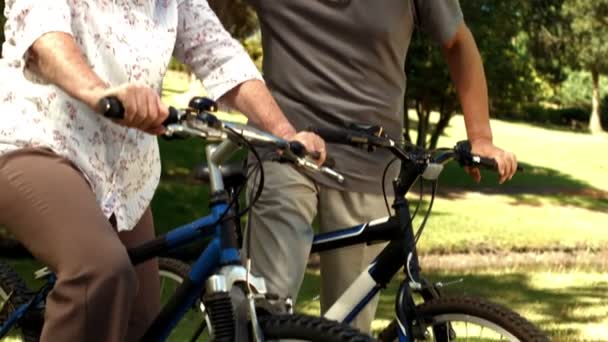 Pareja mayor montando bicicletas en el parque — Vídeos de Stock