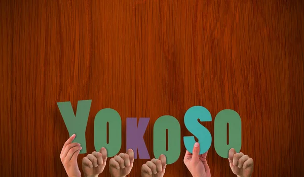 Hands holding up yokoso against oak table — Stock Photo, Image