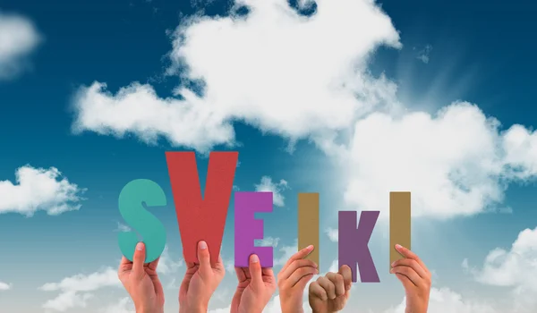 Händer som håller upp sveiki mot blå himmel — Stockfoto