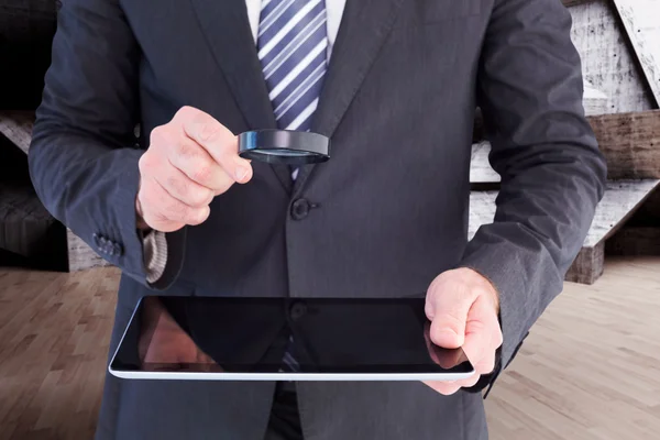 Businessman looking at tablet with magnifying glass — Stock Photo, Image