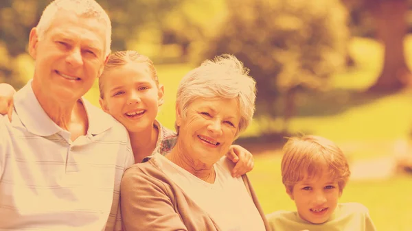 Smiling senior couple and grandchildren at park — Stock Photo, Image