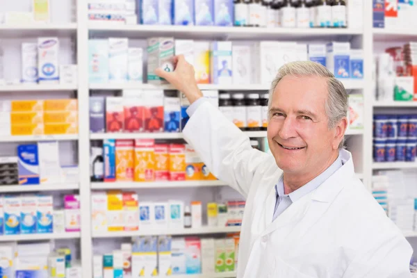 Farmacéutico sonriente tomando medicamentos de la estantería —  Fotos de Stock