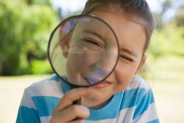 Cute little girl looking through magnifying glass — Stock Photo, Image