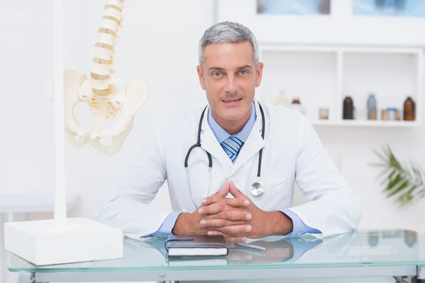 Doctor sentado en su escritorio sonriendo a la cámara — Foto de Stock