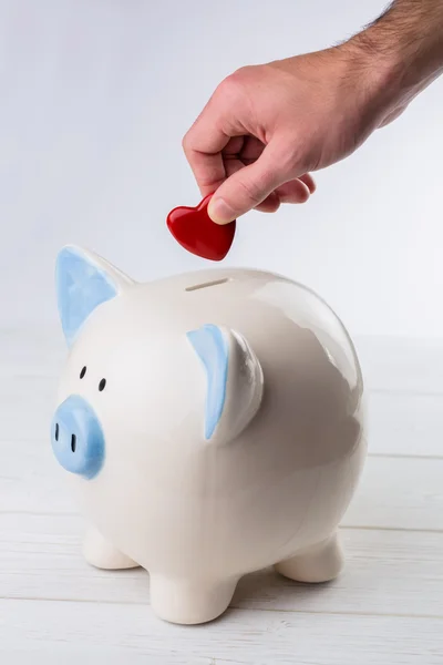 Mão colocando coração no banco porquinho — Fotografia de Stock