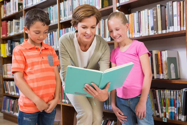 Leraar lezen boek met leerlingen in bibliotheek — Stockfoto