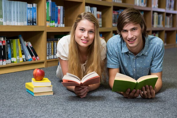 Estudantes lendo livro no chão da biblioteca — Fotografia de Stock