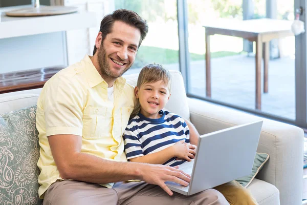 Отец и сын используют ноутбук на диване — стоковое фото
