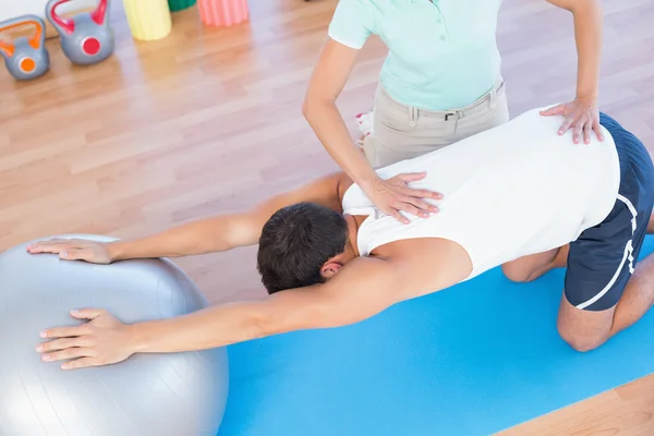 Trainer helping man with exercise ball — Stock Photo, Image