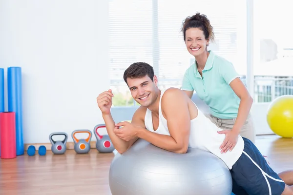 Trainer helping man with exercise ball Stock Photo