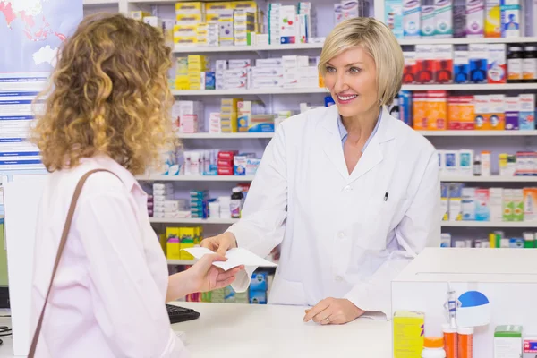 Customer handing a prescription to a smiling pharmacist — Stock Photo, Image