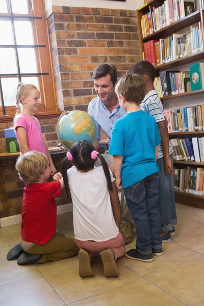 Cute pupils and teacher looking at globe in library — Stock Photo, Image