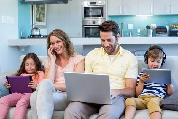 Família feliz no sofá juntos usando dispositivos — Fotografia de Stock