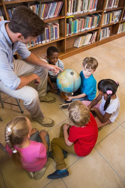 Cute pupils and teacher looking at globe — Stock Photo, Image