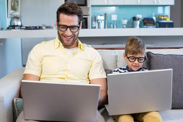 Father and son using laptops on the couch — Stock Photo, Image