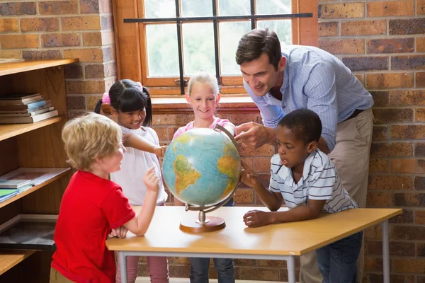 Aranyos tanulók és a tanár nézett globe-könyvtár — Stock Fotó