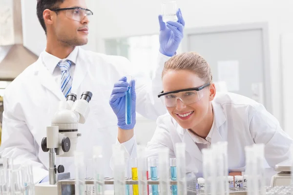 Científicos sonrientes examinan tubo de ensayo y vaso de precipitados — Foto de Stock