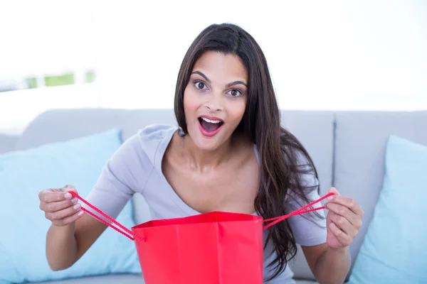 Sonriente hermosa morena sentada en el sofá con ba de compras —  Fotos de Stock