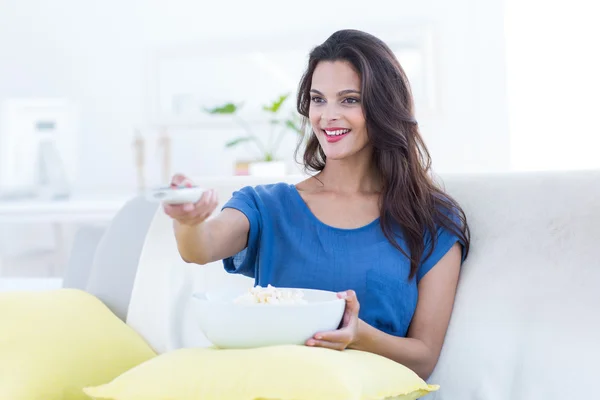 Smiling beautiful brunette relaxing on the couch with bowl of po — Stock Photo, Image