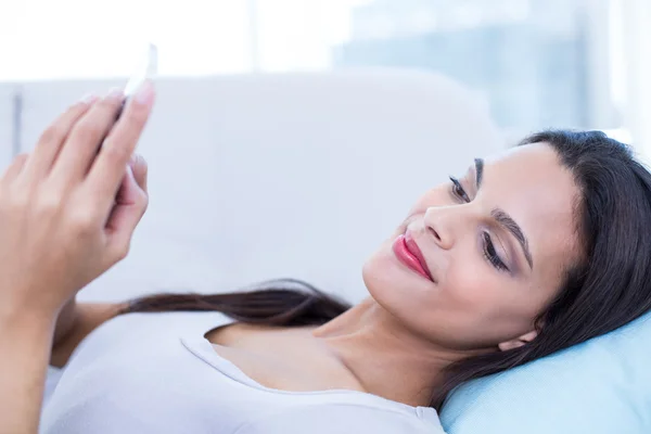 Smiling beautiful brunette relaxing on the couch and using her p — Stock Photo, Image