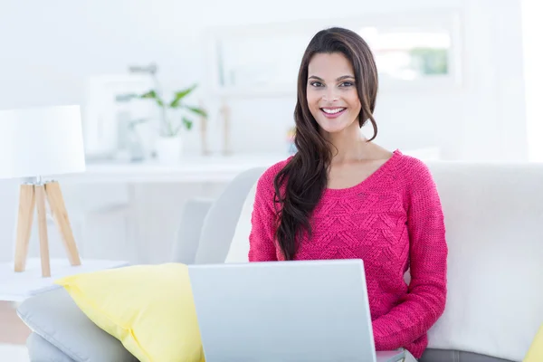 Lächelnd schöne Brünette mit ihrem Laptop auf der Couch — Stockfoto