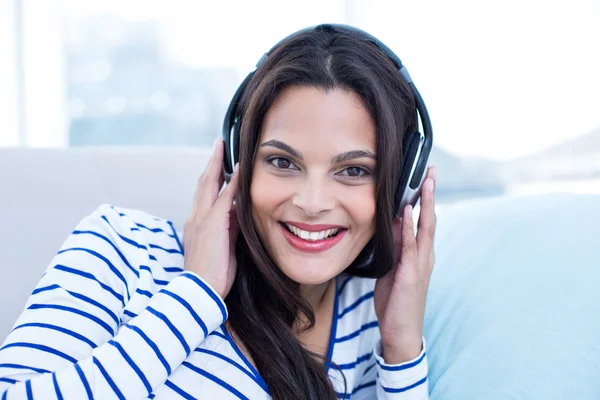 Sorrindo bela morena relaxante no sofá e ouvindo m — Fotografia de Stock