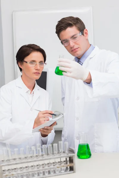 Scientists examining beaker with green fluid — Stock Photo, Image