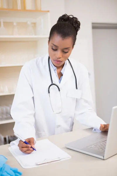 Scientist taking notes while using laptop — Stock Photo, Image