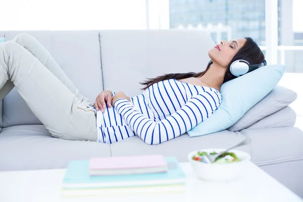 Sonriendo hermosa morena relajándose en el sofá y escuchando m — Foto de Stock