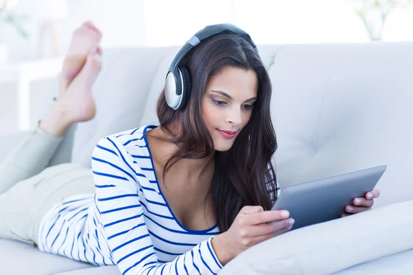 Uśmiechający się piękna brunetka słuchania muzyki podczas korzystania z jej tabeli — Zdjęcie stockowe