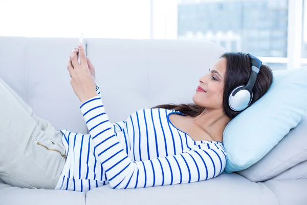 Usmívající se krásná brunetka relaxační na gauči a naslouchající m — Stock fotografie