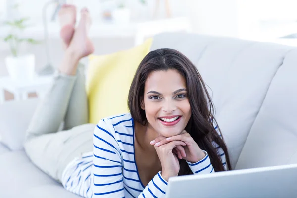 Sonriendo hermosa morena relajándose en el sofá y usando su l —  Fotos de Stock