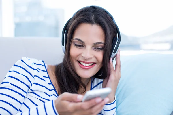 Sorrindo bela morena relaxante no sofá e ouvindo m — Fotografia de Stock