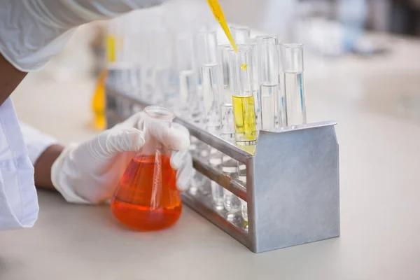 Scientist pouring orange fluid in test tube — Stock Photo, Image