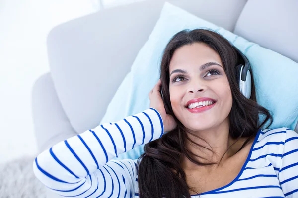 Sorrindo bela morena relaxante no sofá e ouvindo m — Fotografia de Stock