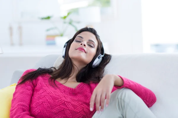 Lächelnd schöne Brünette entspannt sich auf der Couch und lauscht m — Stockfoto