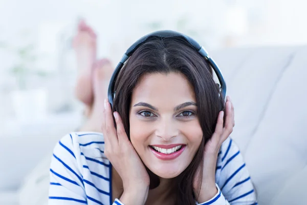 Lächelnd schöne Brünette entspannt sich auf der Couch und lauscht m — Stockfoto